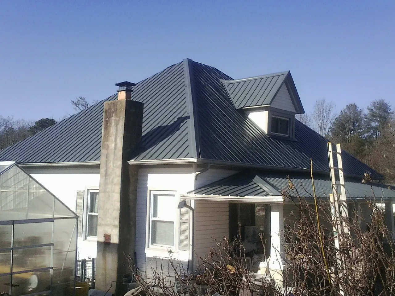 Dark blue standing seam metal roof on a white farmhouse with dormer — Slate & Tile Roof Repair by Roofing Brothers in Montevideo