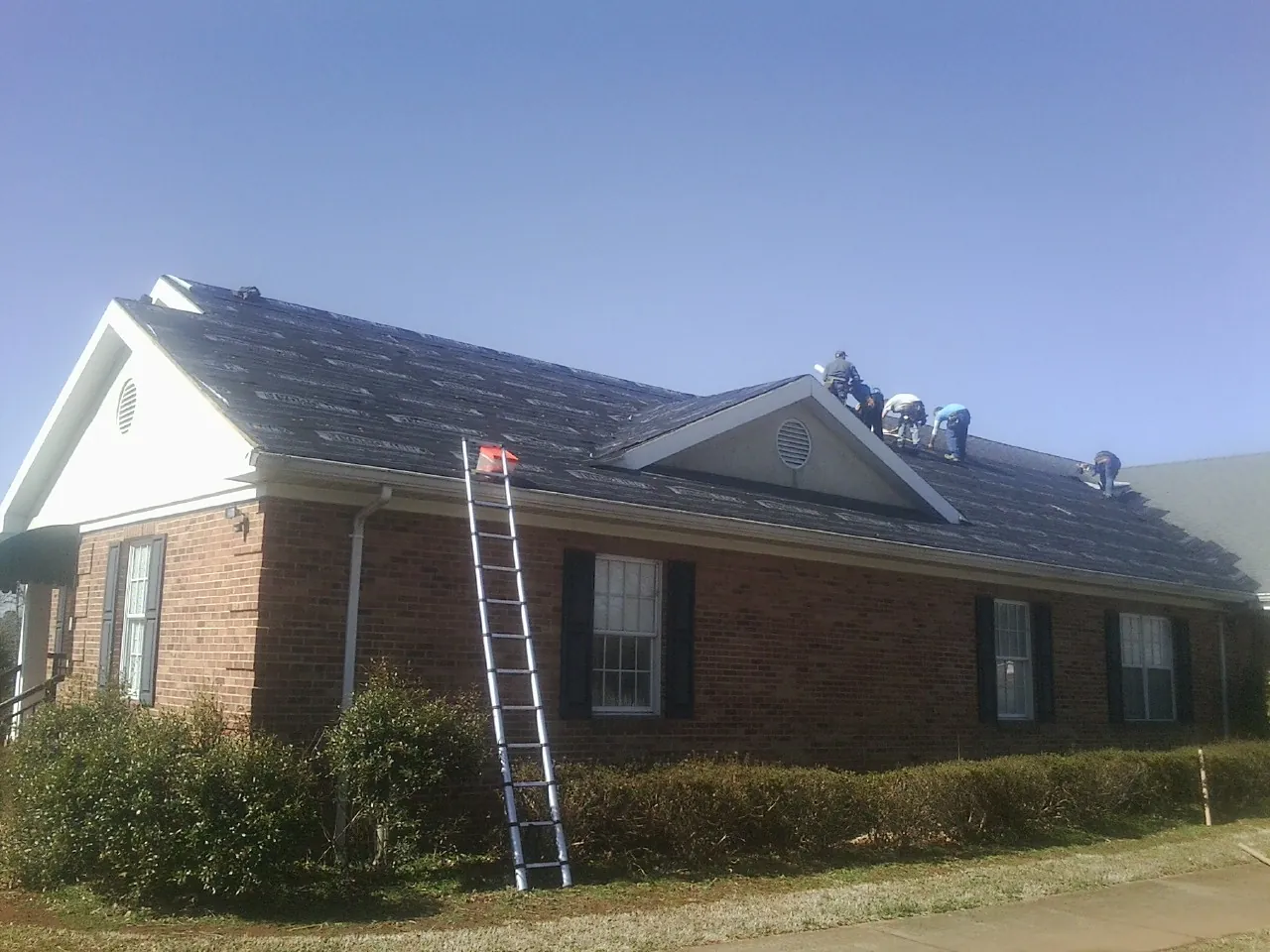 Crew tearing shingles off a brick ranch roof with a ladder set — Emergency Roof Repair work by our crew in Montevideo