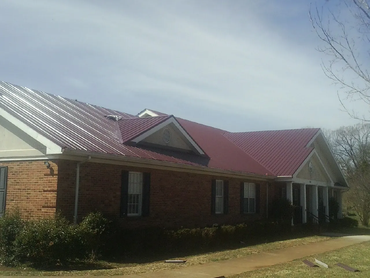 Red metal roof with gabled entries on a long brick building, from a Hail Damage Roof Repair job in Montevideo