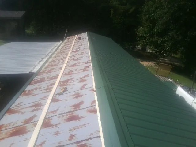 Old rusted panels beside newly installed green metal roofing — Wind Damage Roof Repair by Roofing Brothers in Montevideo