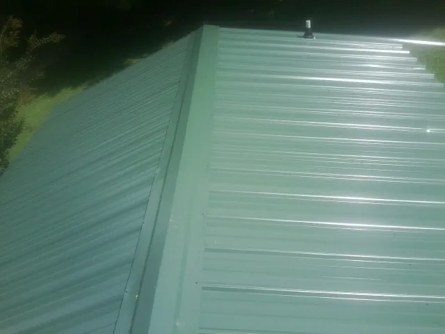 New green metal panels meeting at the ridge of a roof — Flat Roof Repair work by our crew in Montevideo