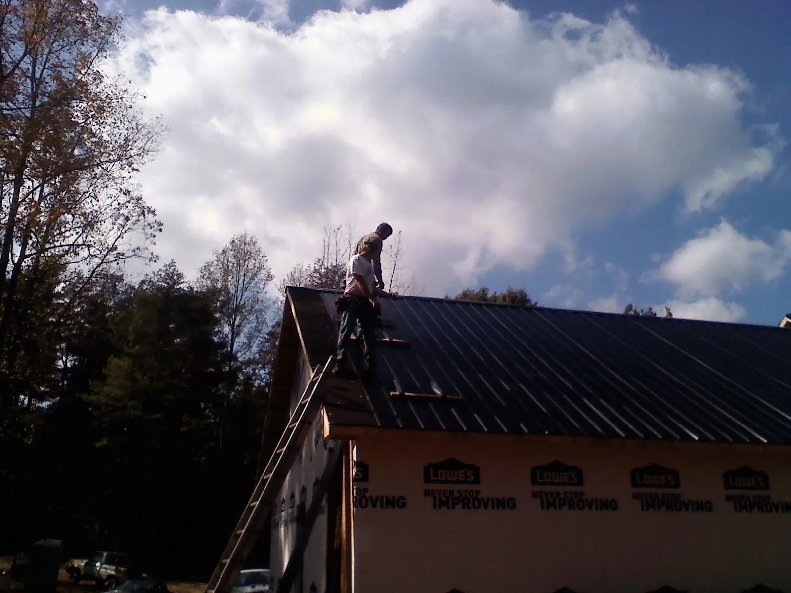 Roofer fastening dark metal panels high against a cloudy sky, from a Roof Inspection job in Montevideo