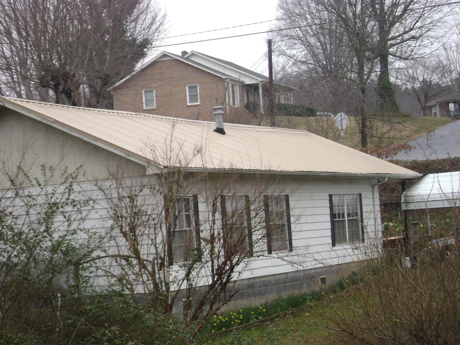 Tan metal roof on a white sided house set into a hillside — Commercial Roofing by Roofing Brothers in Montevideo