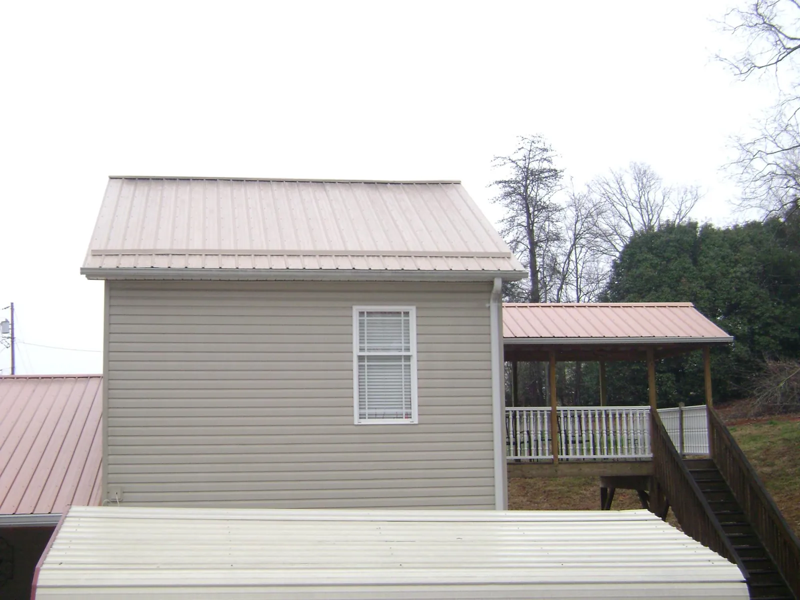 Tan metal roofs on a two story addition and attached porch, from a Roof Replacement job in Montevideo